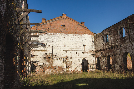 Ruins of an old industrial building made of brick, with large empty rooms, cracked walls, and broken window frames. In a state of disrepair and no longer in use.