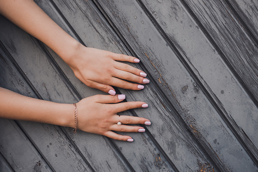 girl shows her beautiful pink manicure on a background of gray gates from diagonal wooden boards. ring on a finger. gold bracelet on the hand.