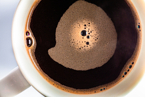 High angle close up of bubbles in a cup of freshly made black coffee.