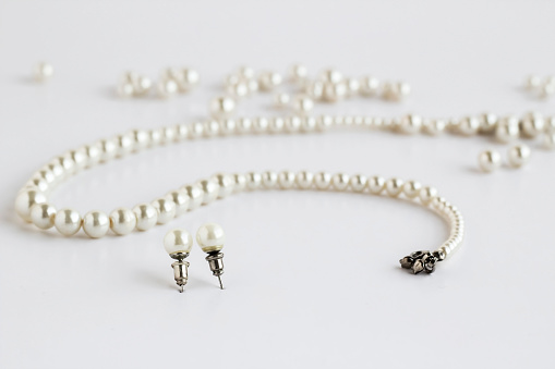 Stylish,pearl necklace on the white surface with a pair of earrings and scattered pearl grains.Mother's Day or any special day concept.