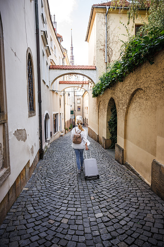 Woman traveler with suitcase and backpack walking on street. Travel and vacation in european city Olomouc, Czech Republic