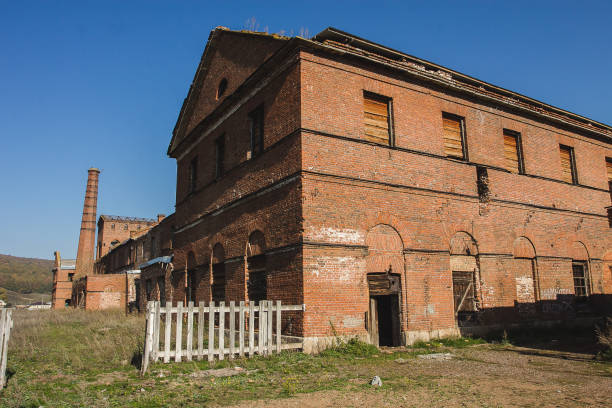 istock Abandoned factory with boarded up windows, overgrown plants and broken fence 1998483045