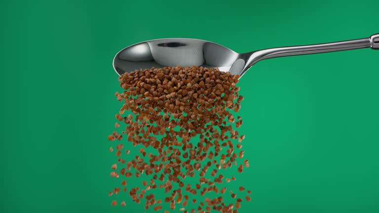 Super slow motion pile of raw brown buckwheat groats grain spilling from a spoon