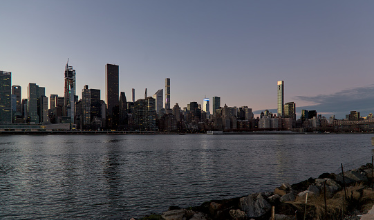 manhattan skyline at sunset (tall residential and commercial buildings) east side midtown and downtown view (dusk on east river) from gantry park in queens nyc