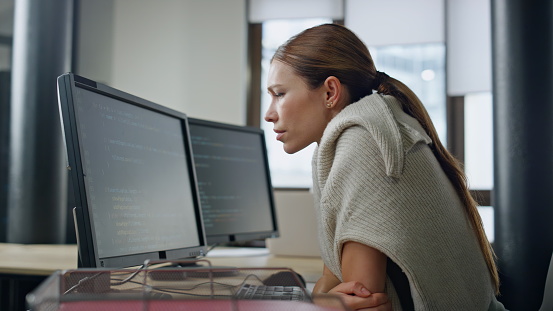 Exhausted developer working office alone. Stressed woman rubbing head searching problem solution. Worried programmer looking software code checking mistakes. Concerned it employee analyzing bug issue