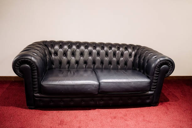 istock Elegant black leather Chesterfield sofa isolated on red background. 1998543700