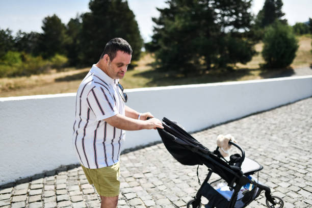 istock Caring Male With Down Syndrome Learning To Push Baby Stroller 1998549628