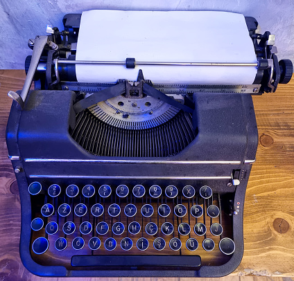 Old vintage typewriter, retro machine with white sheet of paper and typed text \