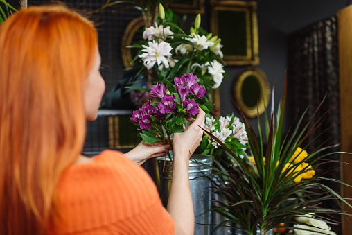 Beautiful redhead female seller working in modern flower shop. She is happy and smiled. Small business concept.