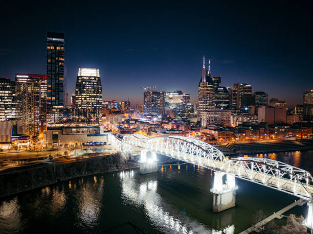 Pedestrian Bridge to Broadway, Downtown Nashville, Tennessee Skyline from the Northeast Bank of the Cumberland River near the Stadium at Dusk Aerial Perspective of Broadway, Downtown Nashville, Tennessee Skyline from the North Bank of the Cumberland River near the Stadium on a Slow Weeknight nashville tennessee bridge stock pictures, royalty-free photos & images