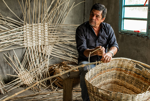 mature latin artisan making wicker baskets in his workshop