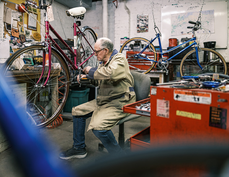 Senior man working in his bicycle shop. He is dressed in casual work clothes. Interior of bicycle shop in Hamilton, Canada.