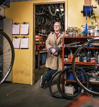 Senior man portrait in his bicycle shop. He is dressed in casual work clothes. Interior of bicycle shop in Hamilton, Canada.