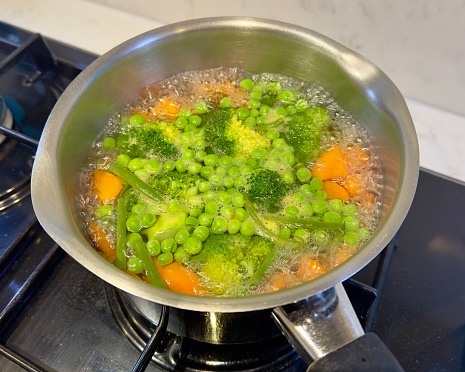 Mixed vegetables cooking in a saucepan on a gas cooker.
