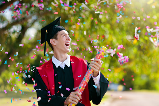 School or college graduation ceremony. Young man in academic regalia, gown and cap, celebration successful diploma certificate. High school graduate in robe, stole and mortar board.