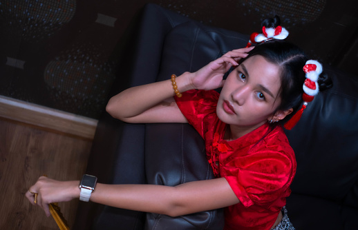 A beautiful woman wearing a red cheongsam uses her left hand and feet wide and looks at you. Sitting on the sofa with a solemn expression Very cool from being the local mafia. Looks very charming.