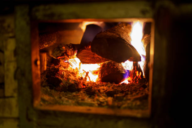 Close-up as a man carefully adds a log to the fire in a woodburning stove.