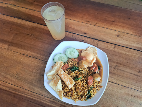 Nyemek Fried Noodle Or Mie Goreng Nyemek With Meatball, Sausage, Fried Dumplings, Cucumber Sliced, Green Mustard And Lime Iced Drink. Mi Goreng Nyemek Dan Es Jeruk Nipis. Food And Drink. Indonesian Food. Restaurant Menu.