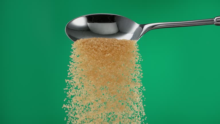 Super slow motion pile of brown sugar spilling from a silver spoon