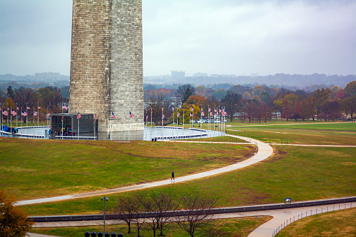 The base of the Washington Monument in the fall, with beautiful fall foliage and American flags in Washington, DC on a gray cloudy day.