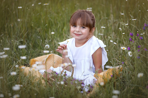Little girl with a bouquet of daisies in summer on a green natural background. Happy child, hidden face, no face, covered with flowers. Copy space. Authenticity, rural life, eco-friendly