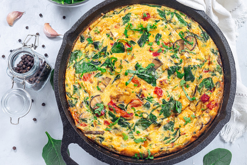 Brunch egg frittata with spinach, roasted red peppers, mushrooms, cheese and herbs, in cast iron skillet, horizontal, top view