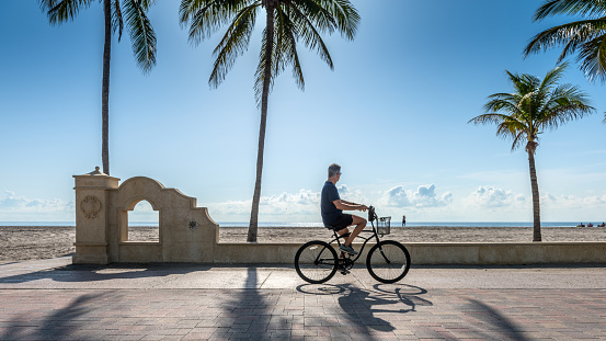 Hollywood Beach, Florida, USA - April 26, 2023: A cyclist rides along the promenade on a sunny morning next to Hollywood Beach in Florida.