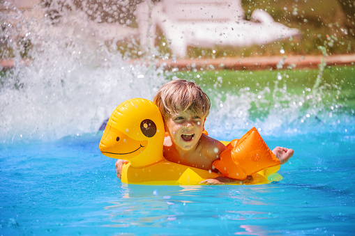 Splashing playfully, a boy of four years old laugh in the cool waters on a striking yellow duckie float during his summer vacations