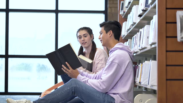 Two high school students in library looking at book