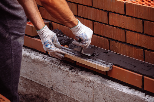 Builder trowels smears cement mortar on brick during bricklaying.