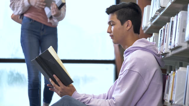 Two high school students in library looking at book