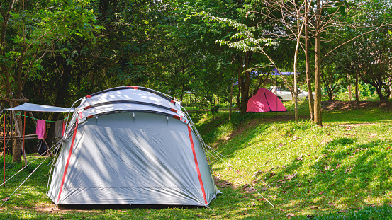 Two field tents on green lawn with sunlight and shade in camping area at natural parkland