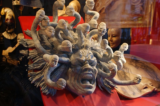 The image appears to depict a dramatic and intricate sculpture featuring multiple anguished figures with outstretched arms, emanating from the central figure resembling a furious, open-mouthed entity. The sculpture is rich in detail and expression, suggesting a theme of intensity or horror. Behind the sculpture, there's a glimpse of other items that could suggest this is an exhibit or a collection of some sort.