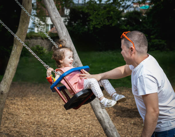 istock A man pushes a child on a swing in a park on a summer day. 1999066428