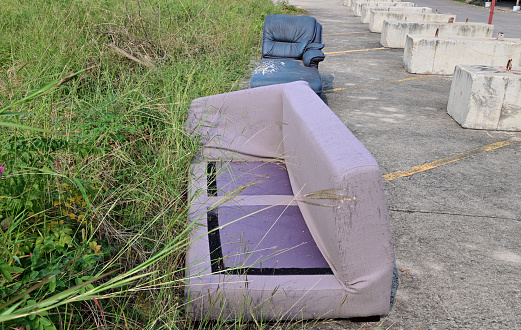 Closeup of Dirty Old Colorful Sofa is left with garbage on the side of the road with natural background at Thailand.