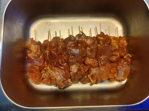 Raw chicken meat and yakitori chicken thigh skewers lie in an iron food container and are ready to be fried on a grill, barbecue or teriyaki plate in an all you can eat world restaurant. There are no recognizable persons or trademarks in the shot.