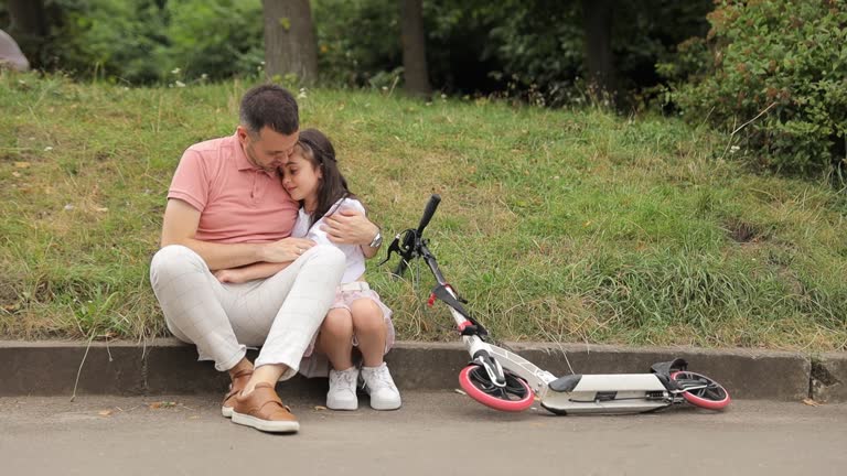 A man and a woman are sitting on the curb next to a scooter