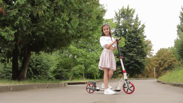 Young girl happily rides scooter on vibrant city street.