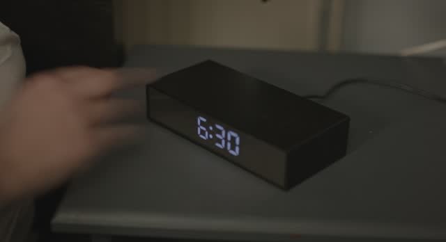 Alarm clock turns to 6:30 in the morning, a woman taps the clock and snoozes the alarm