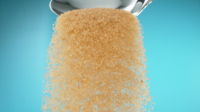 Super slow motion pile of brown sugar spilling from a metal spoon