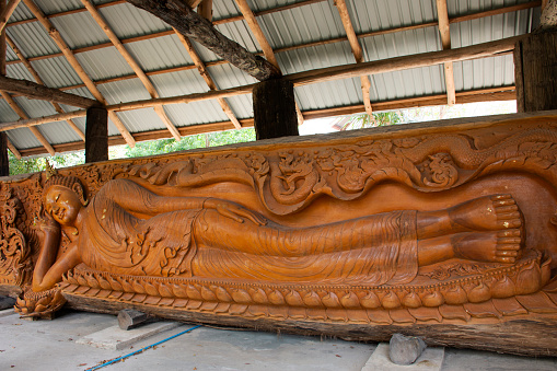 Art sculpture carving wooden ancient buddha reclining statue for thai people traveler travel visit and respect praying blessing of Wat Tham Khao Prathun Temple at Ban Rai city in Uthai Thani, Thailand