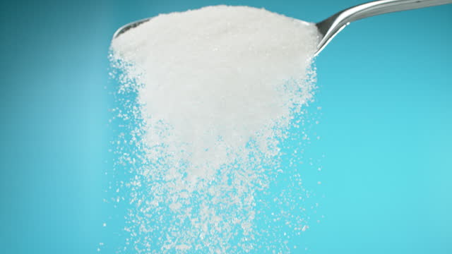 Super slow motion white ground sugar falling from a spoon