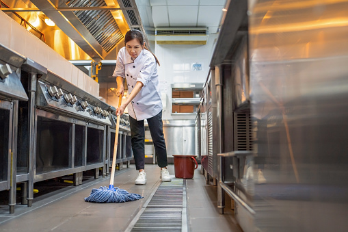 female restaurant worker mopping the floor, cleaning commercial kitchen after used