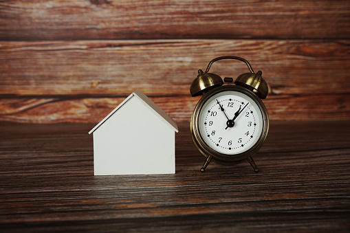 House model with alarm clock on wooden background