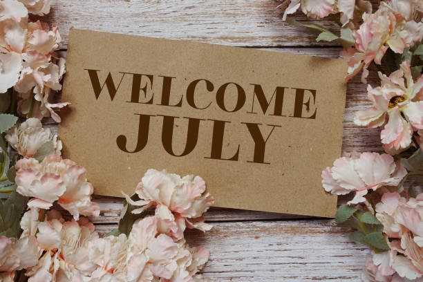 istock Welcome July typography text with flowers frame on wooden background 1999395929