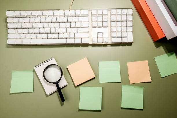 istock Closeup view of magnifying glass and computer keyboard with an empty notebook and note paper 1999410899