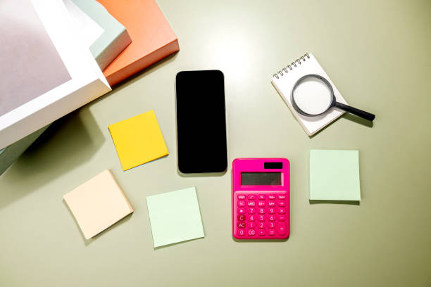 istock Closeup view of mobile phone with blank screen and an empty notebook and note paper with magnifying glass and calculator 1999414531