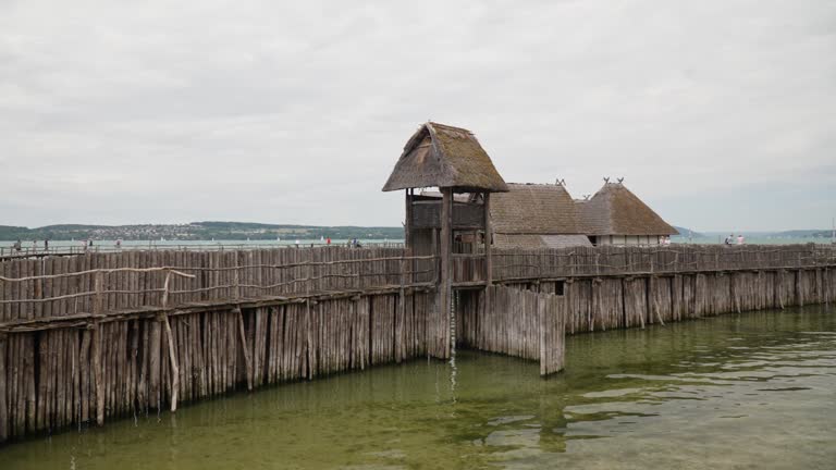 Thatched-roof structures on stilts over water, reminiscent of prehistoric dwellings, cloudy day