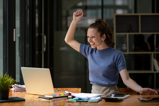 Happy business woman celebrating victory while receiving good news on her laptop, excited about success.