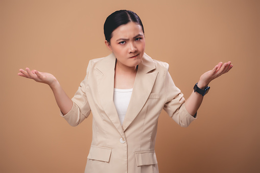 Asian woman angry annoyed and shrugging shoulders standing isolated over beige background.